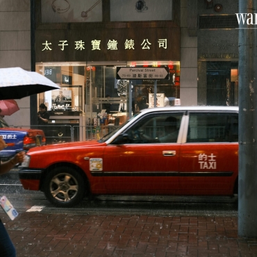 A tourist with an umbrella walks on a wet cobblestone street during a rainy day in China.